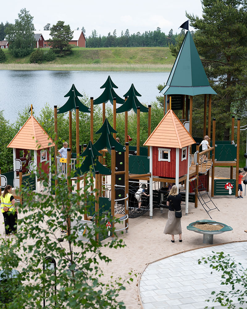 Large playground unit with forest theming, nestled amongst trees next to a large Swedish lake.